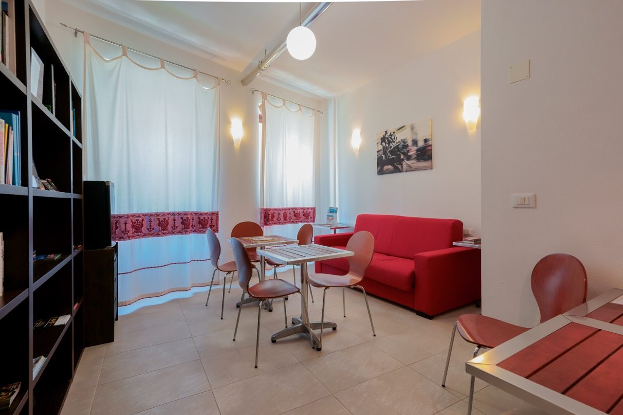 The Saletta common room at Le Suite sul Corso: red sofa and tables